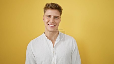 Lachender, selbstbewusster junger Kaukasier in lässiger Manier, isoliert vor gelbem Hintergrund stehend, der positive Stimmung und Freude ausstrahlt