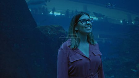 Photo for A smiling young woman enjoys the view at an aquarium in dubai, with marine life visible through the glass. - Royalty Free Image