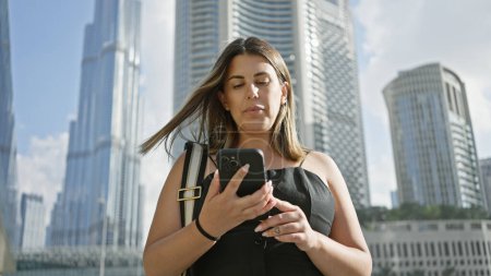 Téléchargez les photos : Une jeune femme utilise un smartphone avec des gratte-ciel de dubai en arrière-plan. - en image libre de droit