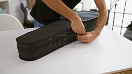 Talented hispanic male musician's hands captured opening acoustic violin case for intense practice session inside buzzing music studio