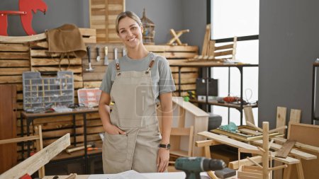 Photo for Smiling confident young woman standing in a carpentry studio surrounded by woodwork tools - Royalty Free Image