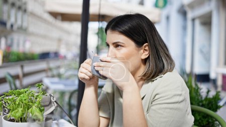 Téléchargez les photos : Jeune belle femme hispanique buvant du café assis sur la table à la cafétéria extérieure - en image libre de droit