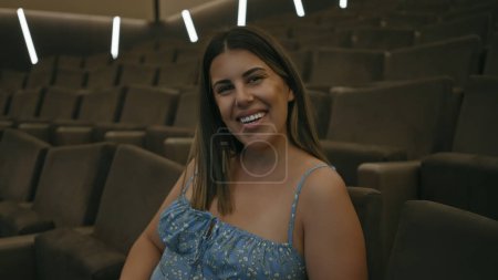 Téléchargez les photos : Femme souriante assise seule dans une salle de cinéma avec des sièges vides autour d'elle - en image libre de droit