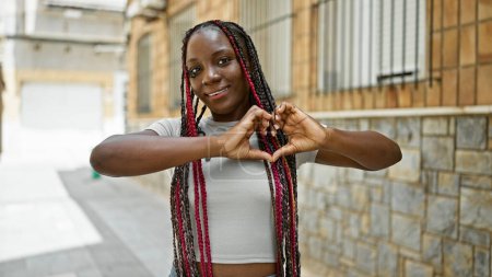 Photo for Happy african american woman making lovely heart sign with hands on urban street, radiating joy and confidence - Royalty Free Image