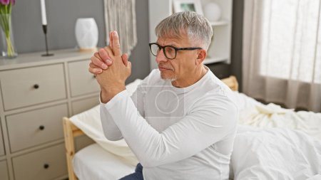 Ein Mann mittleren Alters gestikuliert mit den Händen, die eine Waffe in einem modernen Schlafzimmer imitieren.