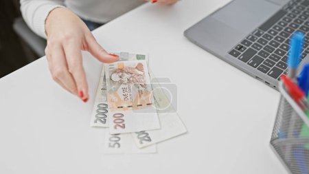 Czech currency handled by a businesswoman at a laptop in an office setting, evoking themes of finance and technology.