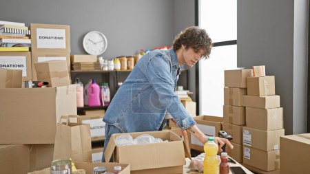 Photo for Handsome young man packing donations in a room filled with cardboard boxes and household items. - Royalty Free Image