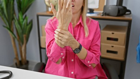A young woman experiencing wrist pain in a modern office setting, depicting a healthcare or occupational concept.