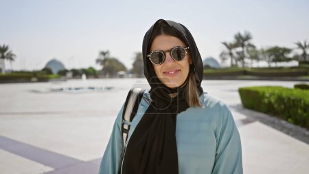 Porträt einer lächelnden jungen Frau mit Sonnenbrille und Hijab in einer islamischen Moschee in Abu dhabi, uae.