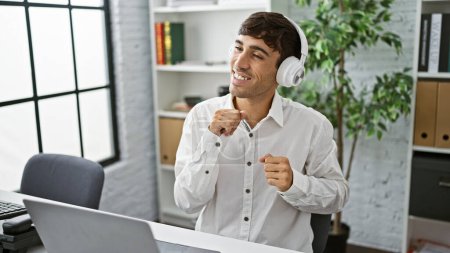 Young hispanic man and business worker jamming to music and dancing in the office, embodying the spirit of success and work joy