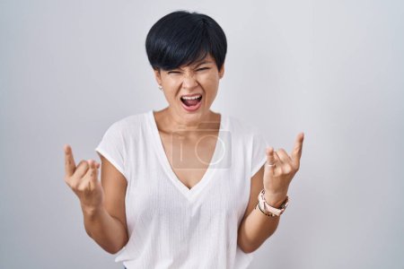 Photo for Young asian woman with short hair standing over isolated background shouting with crazy expression doing rock symbol with hands up. music star. heavy music concept. - Royalty Free Image