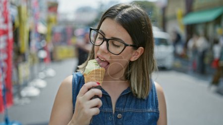Téléchargez les photos : Femme hispanique joyeuse et belle dans des lunettes savoure joyeusement un délicieux cône de crème glacée au milieu du marché extérieur tsukiji animé - pour s'amuser en été! - en image libre de droit