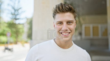 Photo for Confident young caucasian man, sporting casual look, caught smiling standing on a bustling street in the outdoors of the city, spreading positivity, joy, and the coolest, laid-back vibe. - Royalty Free Image