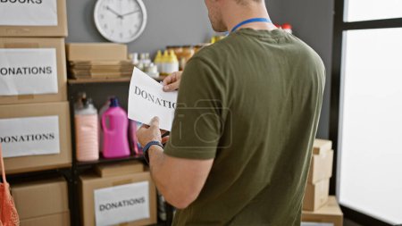 Téléchargez les photos : Un bénévole tenant une pancarte de don dans un entrepôt rempli de fournitures et de boîtes en carton. - en image libre de droit