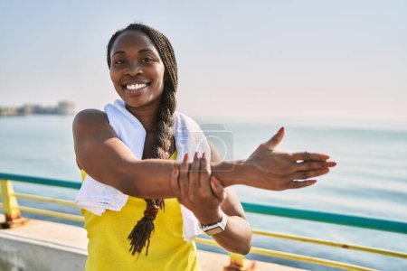 Foto de Mujer afroamericana usando ropa deportiva estirando el brazo a la orilla del mar - Imagen libre de derechos
