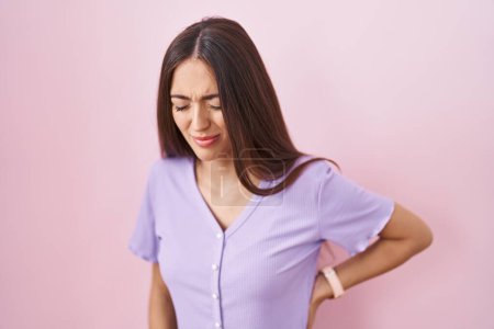 Photo for Young hispanic woman with long hair standing over pink background suffering of backache, touching back with hand, muscular pain - Royalty Free Image