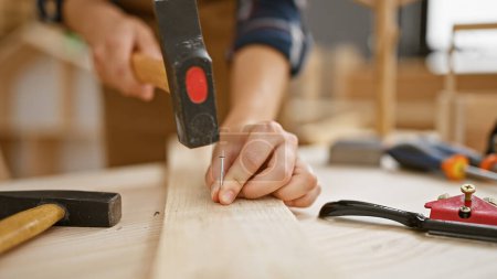Foto de Manos fuertes de carpintero hembra clavan clavo en tablón de madera en taller de carpintería profesional - Imagen libre de derechos