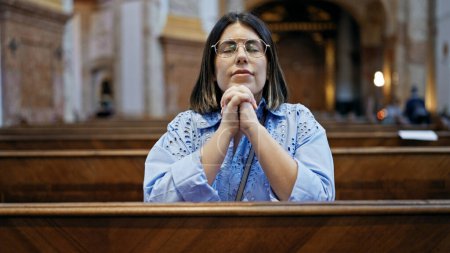 Junge schöne hispanische Frau betet auf einer Kirchenbank in der Kirche St. Karl Borromus 