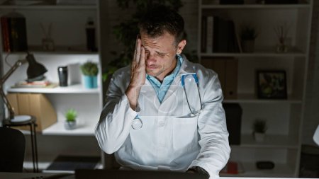 Photo for A stressed doctor in a clinic holding his head in frustration at his workplace. - Royalty Free Image