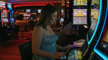 Téléchargez les photos : Femme souriante jouant à une machine à sous dans un casino, environnement de jeu éclairé par des néons colorés. - en image libre de droit