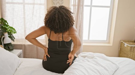 Téléchargez les photos : Femme afro-américaine avec des tresses assises sur le lit dans une chambre - en image libre de droit