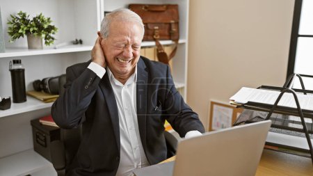 Téléchargez les photos : Stressé homme âgé souffrant de douleur cervicale tout en travaillant intensément sur ordinateur portable au bureau - en image libre de droit