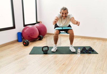 Photo for Middle age grey-haired man smiling confident training leg exercise at sport center - Royalty Free Image