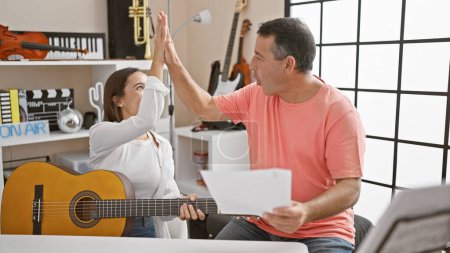 Photo for High-five moment as a confident man and woman musicians share a classic guitar lesson at a buzzing music studio! - Royalty Free Image