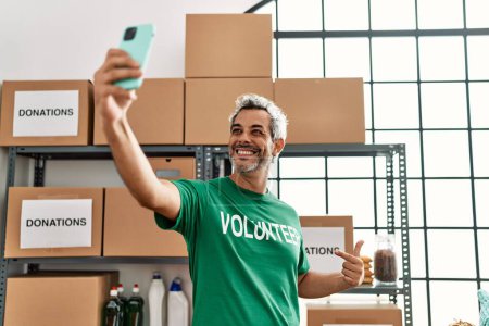 Téléchargez les photos : Middle age grey-haired man volunteer smiling confident make selfie by smartphone at charity center - en image libre de droit