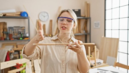 Téléchargez les photos : Femme blonde axée sur la précision dans un atelier de menuiserie ensoleillé portant des lunettes de sécurité. - en image libre de droit