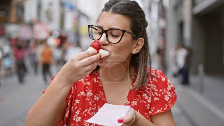 Photo for Gorgeous hispanic girl in specs relishing strawberry japanese mochi on osaka's famous dotonbori street - Royalty Free Image