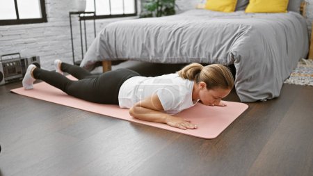 Photo for Beautiful and strong young blonde woman enjoying calm, mindful morning exercise, meditating while powering up with push ups on her bedroom floor for balance and wellness - Royalty Free Image