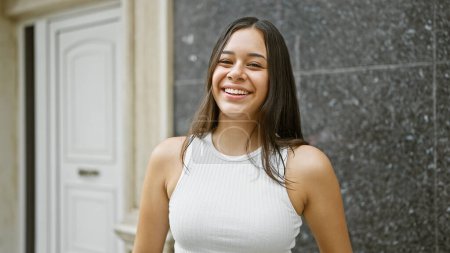 Smiling young hispanic woman full of joy stands confidently on an urban street, her happy expression capturing her cool, casual lifestyle. this beautiful portrait shows her happiness outdoors.