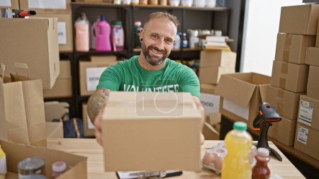 Attraktiver junger Mann in ehrenamtlicher Uniform lächelt selbstbewusst und verteilt Päckchen am Tisch des Charity-Zentrums