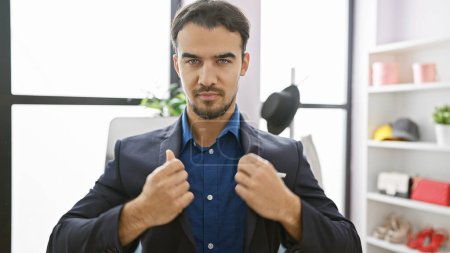 Téléchargez les photos : Bel homme hispanique avec veste de costume ajustable barbe dans un cadre de garde-robe intérieure moderne - en image libre de droit
