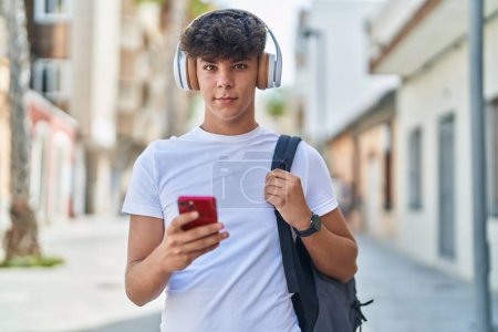 Foto de Joven estudiante adolescente hispano sonriendo confiado escuchando música en la calle - Imagen libre de derechos
