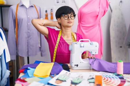 Foto de Middle age chinese woman tailor stressed using sewing machine at atelier - Imagen libre de derechos