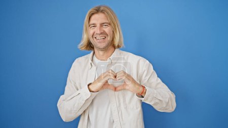 Photo for Cheerful man making heart gesture with hands against blue background - Royalty Free Image