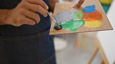 Photo for Close-up of a man's hand mixing paint colors on a palette in an indoor art studio setting. - Royalty Free Image
