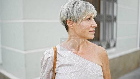 Téléchargez les photos : Femme mûre élégante avec les cheveux gris à l'extérieur dans un cadre urbain regardant loin réfléchie. - en image libre de droit