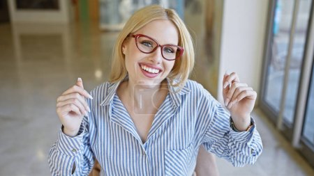 Téléchargez les photos : Une jeune femme caucasienne souriante portant des lunettes et une chemise rayée à l'intérieur avec un fond flou - en image libre de droit