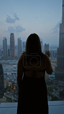 Foto de Una mujer silueta mira el horizonte de Dubái desde un observatorio durante el crepúsculo. - Imagen libre de derechos