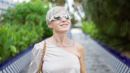 Photo for A confident mature woman enjoys a sunny day outdoors, surrounded by lush greenery in a serene park. - Royalty Free Image