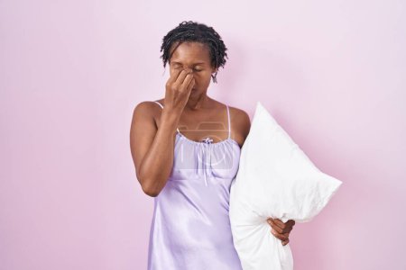 Foto de Mujer africana con rastas usando pijama abrazando almohada cansada frotando nariz y ojos sintiendo fatiga y dolor de cabeza. concepto de estrés y frustración. - Imagen libre de derechos