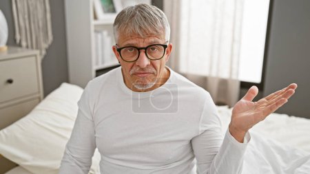 Photo for Middle-aged man with glasses sitting in a bedroom expressing confusion - Royalty Free Image