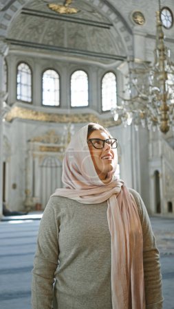 Téléchargez les photos : Femme souriante avec foulard admirant l'intérieur orné d'une mosquée istanbul - en image libre de droit