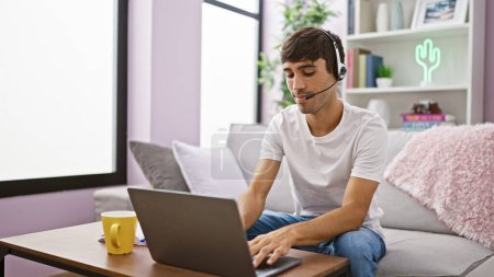 Photo for Young hispanic man call center agent using laptop and headphones sitting on sofa at home - Royalty Free Image