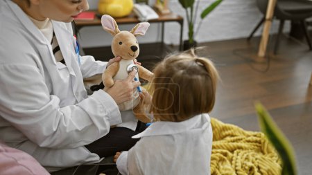 Photo for A woman in a lab coat uses a stethoscope on a toy kangaroo, watched by a child dressed as a doctor in a home setting. - Royalty Free Image