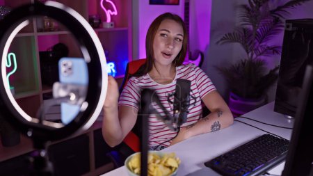 Photo for A young woman streams video games in a neon-lit room at night, with microphone, ring light, and snacks visible. - Royalty Free Image