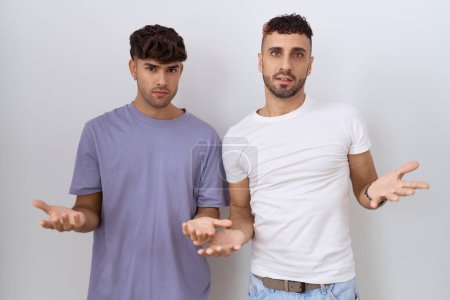 Téléchargez les photos : Homosexuel gay couple debout sur blanc fond sans aucune idée et confus avec ouvert bras, aucune idée concept. - en image libre de droit